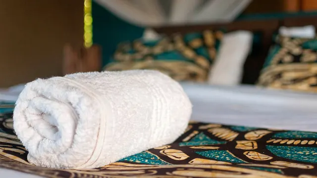 A bed dressed with brightly printed local cotton under a mosquito net, with a rolled white towel laid across it